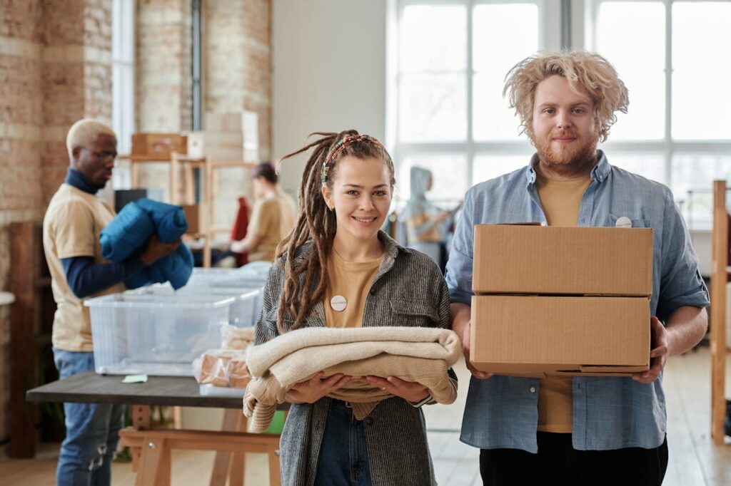 Smiling volunteers holding boxes and clothes, assisting in a donation drive indoors.