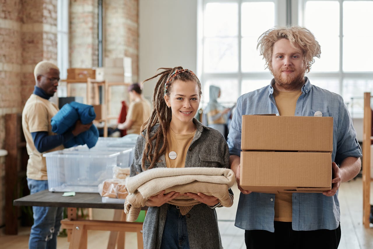 Smiling volunteers holding boxes and clothes, assisting in a donation drive indoors.